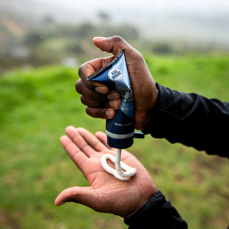 Person applying Ass Magic anti chafe cream for athletes from a tube on a palm in a natural setting.