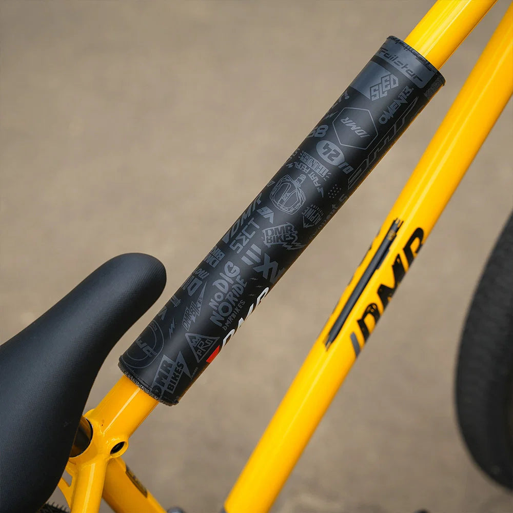 Close-up of DMR BMX bike frame pad on a yellow bike frame, showcasing durable design and logo graphics.