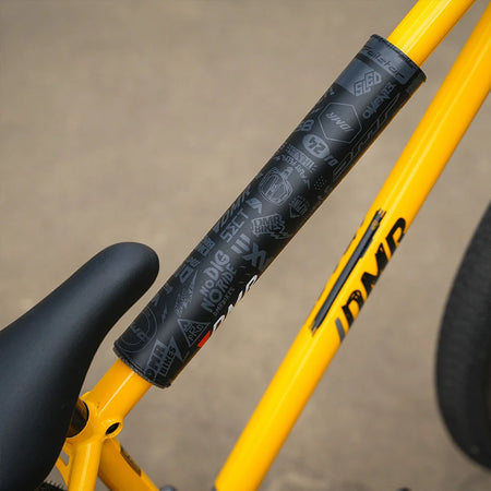 Close-up of DMR BMX bike frame pad on a yellow bike frame, showcasing durable design and logo graphics.