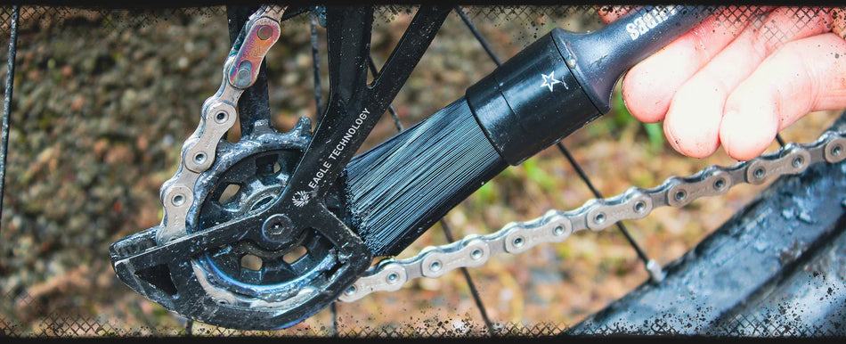 Person using a Juice Lubes Stiffler Drivetrain Brush for bikes to clean a bike chain and chainring.