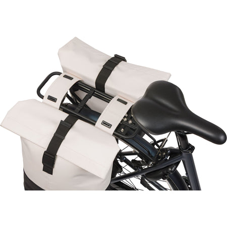 Basil Cove double pannier bag in off-white and black mounted on a bicycle rack.