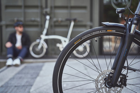 Close-up of Continental Contact urban hybrid bike tyre with urban commuter backdrop.