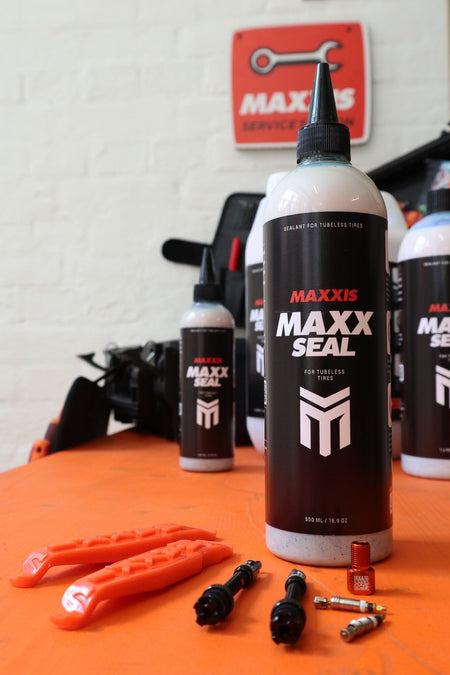 Maxxis Maxx Seal Bicycle Tyre Tubeless Sealant and tools on an orange surface, ideal for Maxxis tubeless tyre sealant application.