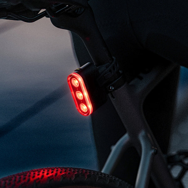 Ravemen TR600 USB rechargeable rear bike light mounted on a bicycle, illuminated in red for visibility.