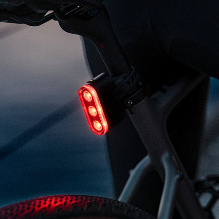 Ravemen TR600 USB rechargeable rear bike light mounted on a bicycle, illuminated in red for visibility.