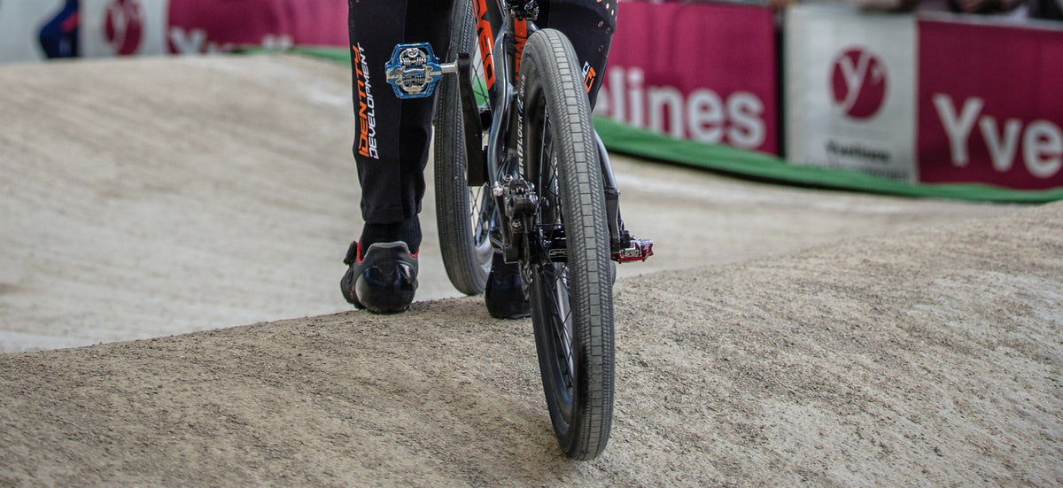 Close-up of a rider's foot on a BMX bike with a Tioga Powerblock 20 inch BMX wired tyre on a dirt track.