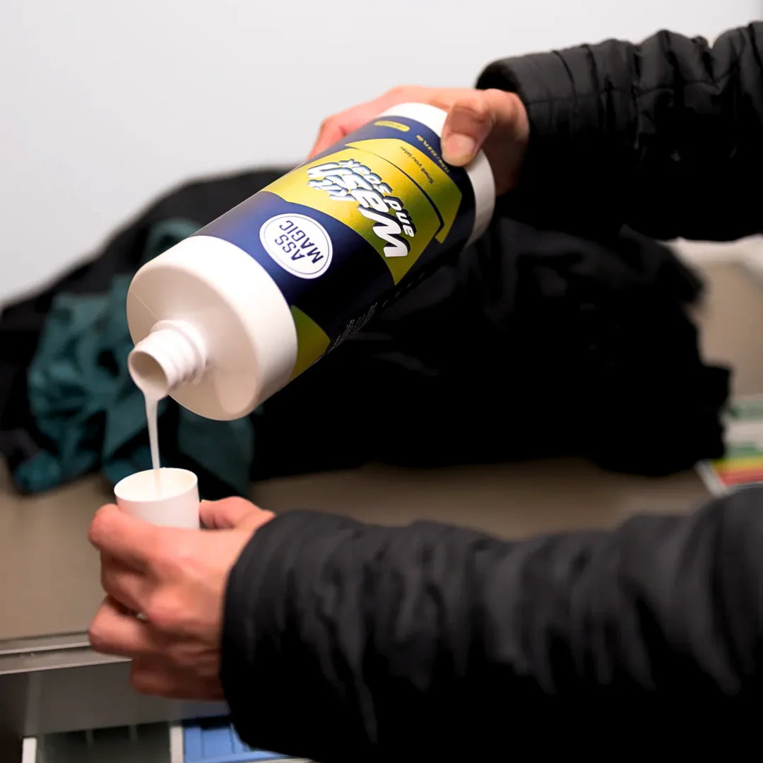 Person pouring Ass Magic enzyme kit sports gear wash into a measuring cup for cleaning sportswear.